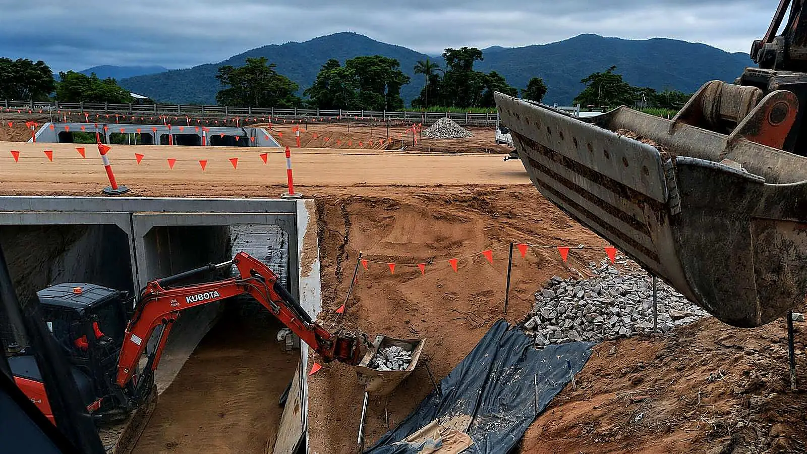 Excavators undertaking earthworks beside a concrete culvert and drainage structure