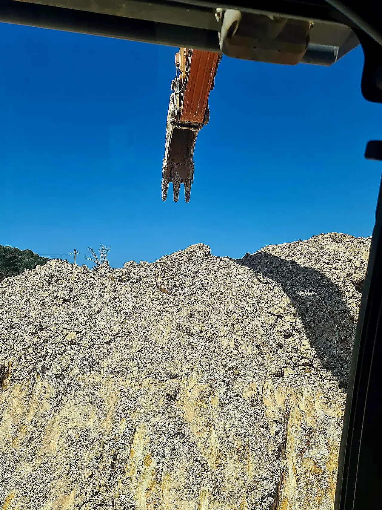 Excavator bucket above a weathered sandstone and clay cut face, photographed from the operator cab on a South East Queensland civil site.