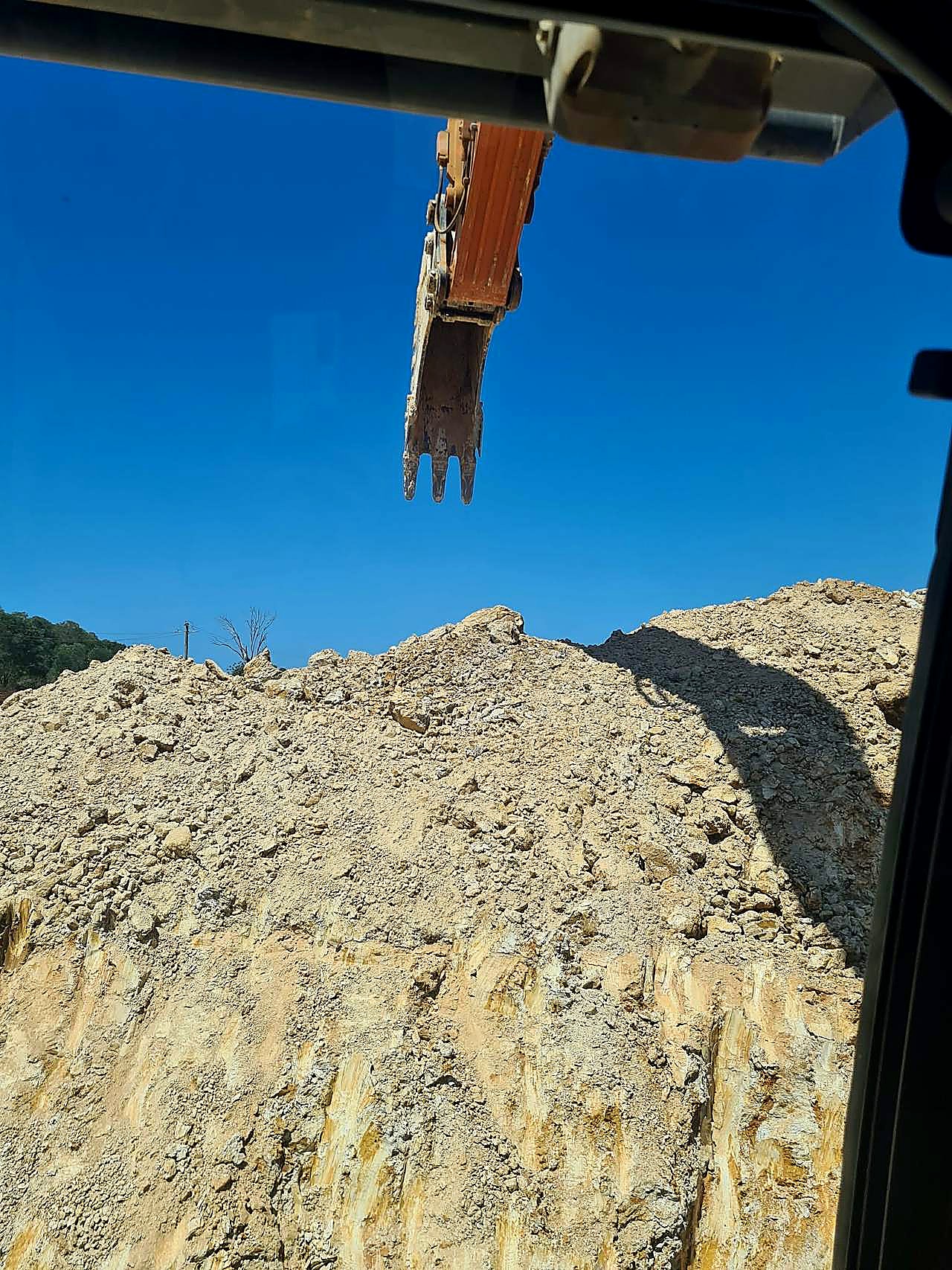 Excavator bucket above a weathered sandstone and clay cut face, photographed from the operator cab on a South East Queensland civil site.