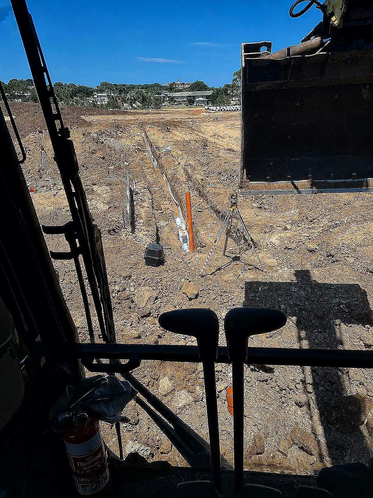 Open gravity trench with pipe laser and survey gear, photographed from the excavator cab on an SEQ civil site
