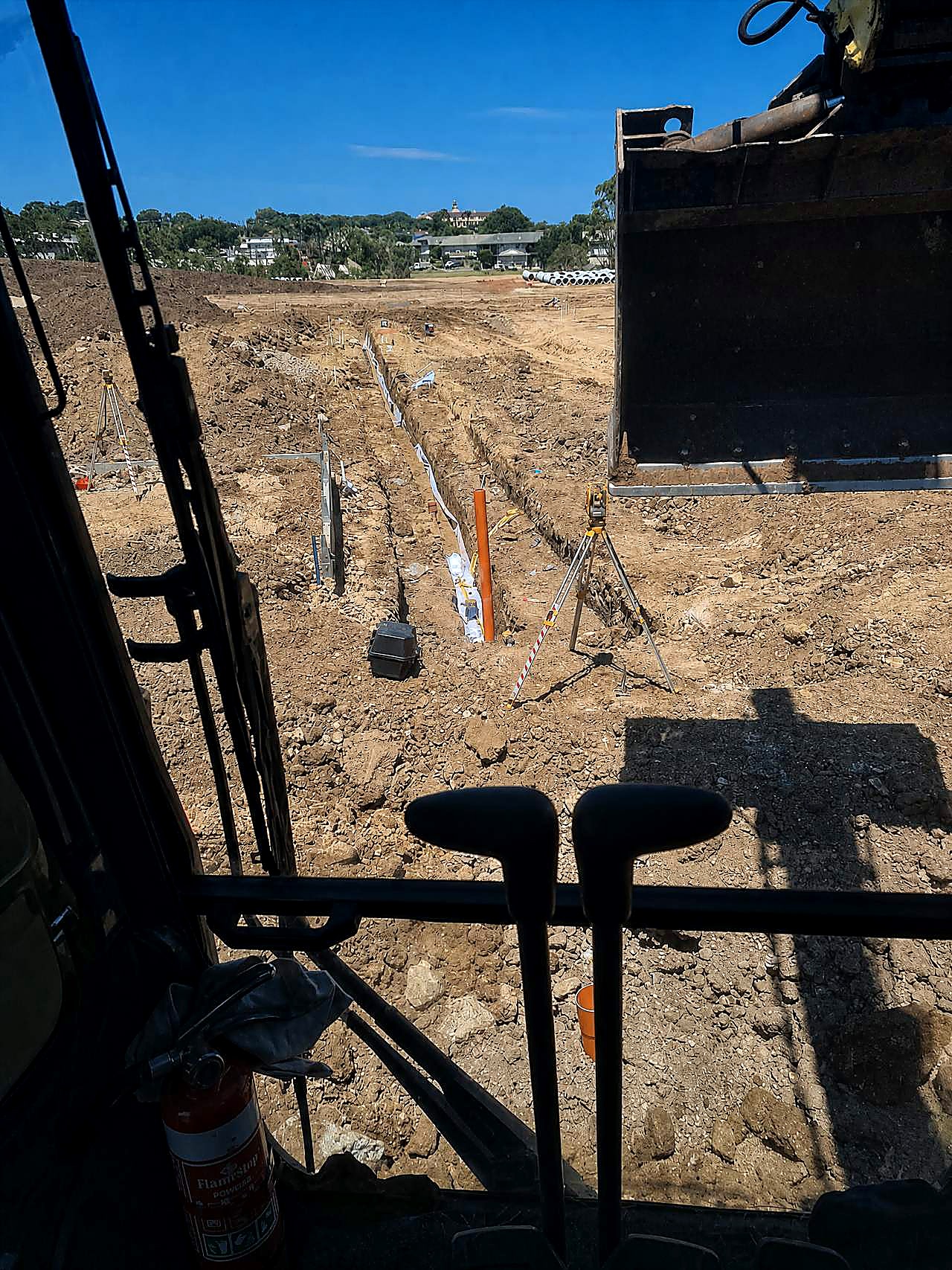 Open gravity trench with pipe laser and survey gear, photographed from the excavator cab on an SEQ civil site